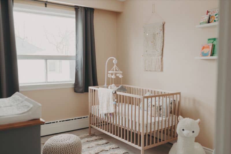 baby room with crib, mobile over crib. walls a soft pink color and gray curtains