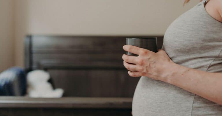profile of pregnant belly with hand holding cup