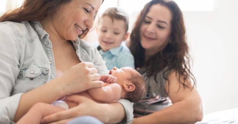 grandma holding newborn in arms with mother and small child looking on