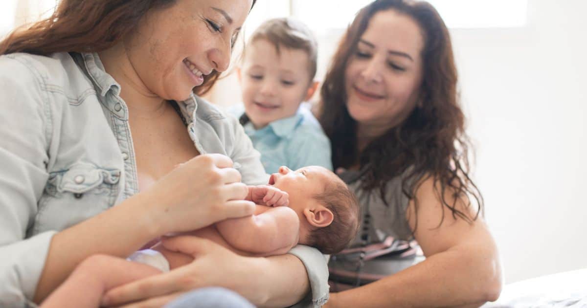 grandma holding newborn in arms with mother and small child looking on
