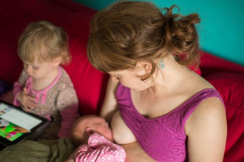 woman breastfeeding baby sitting next to child.  